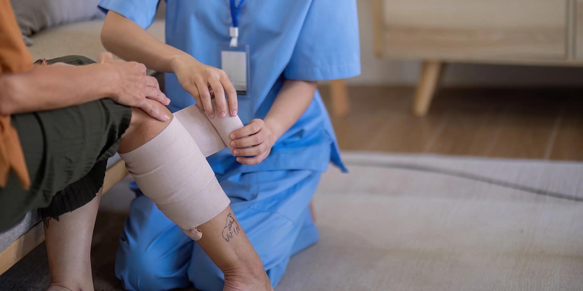 Caregiver bandaging elderly woman's leg